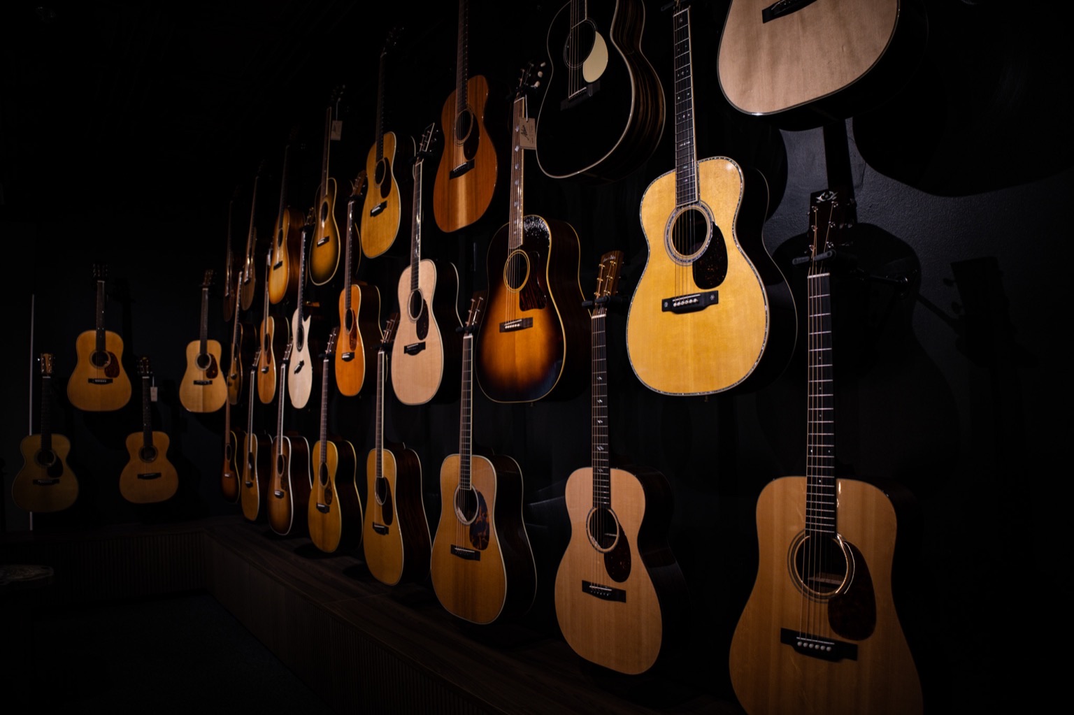 A dimly lit wall of acoustic guitars in the Corzic showroom